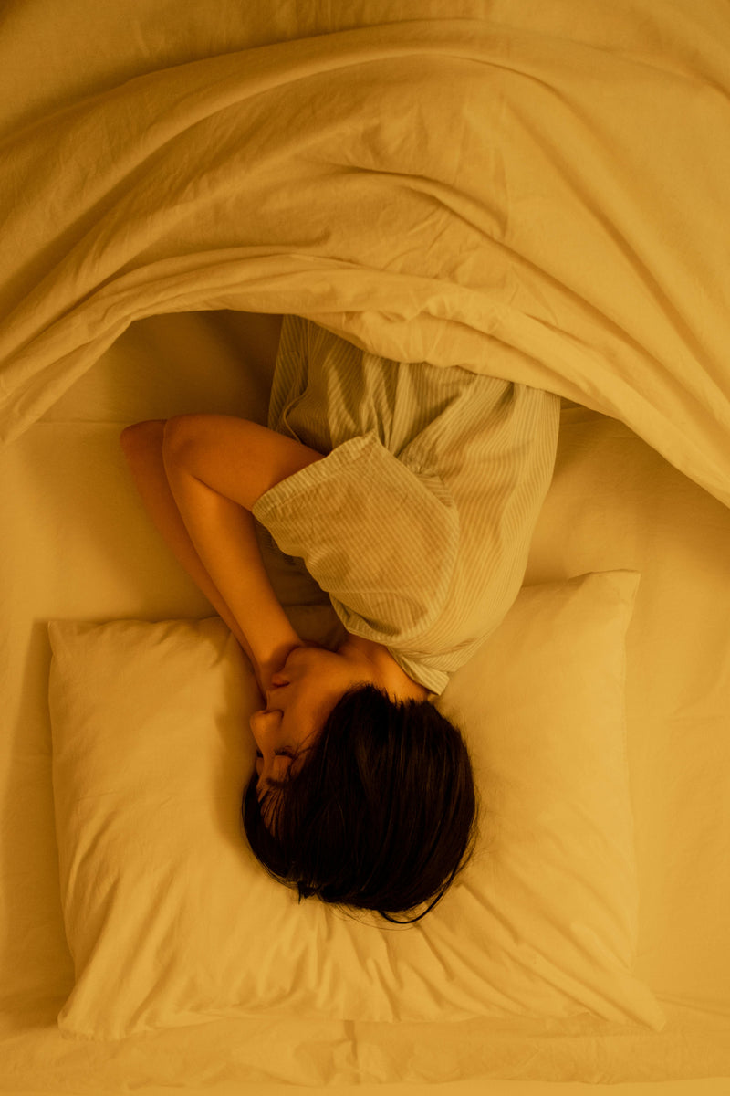 Person lying in bed under a blanket with a warm, yellowish light.